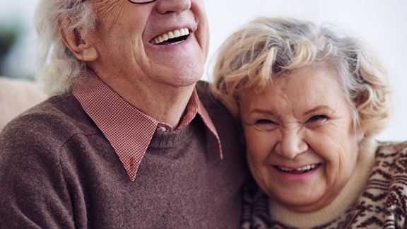 Dos personas mayores sentadas en un sofá sonriendo y agarradas de la mano