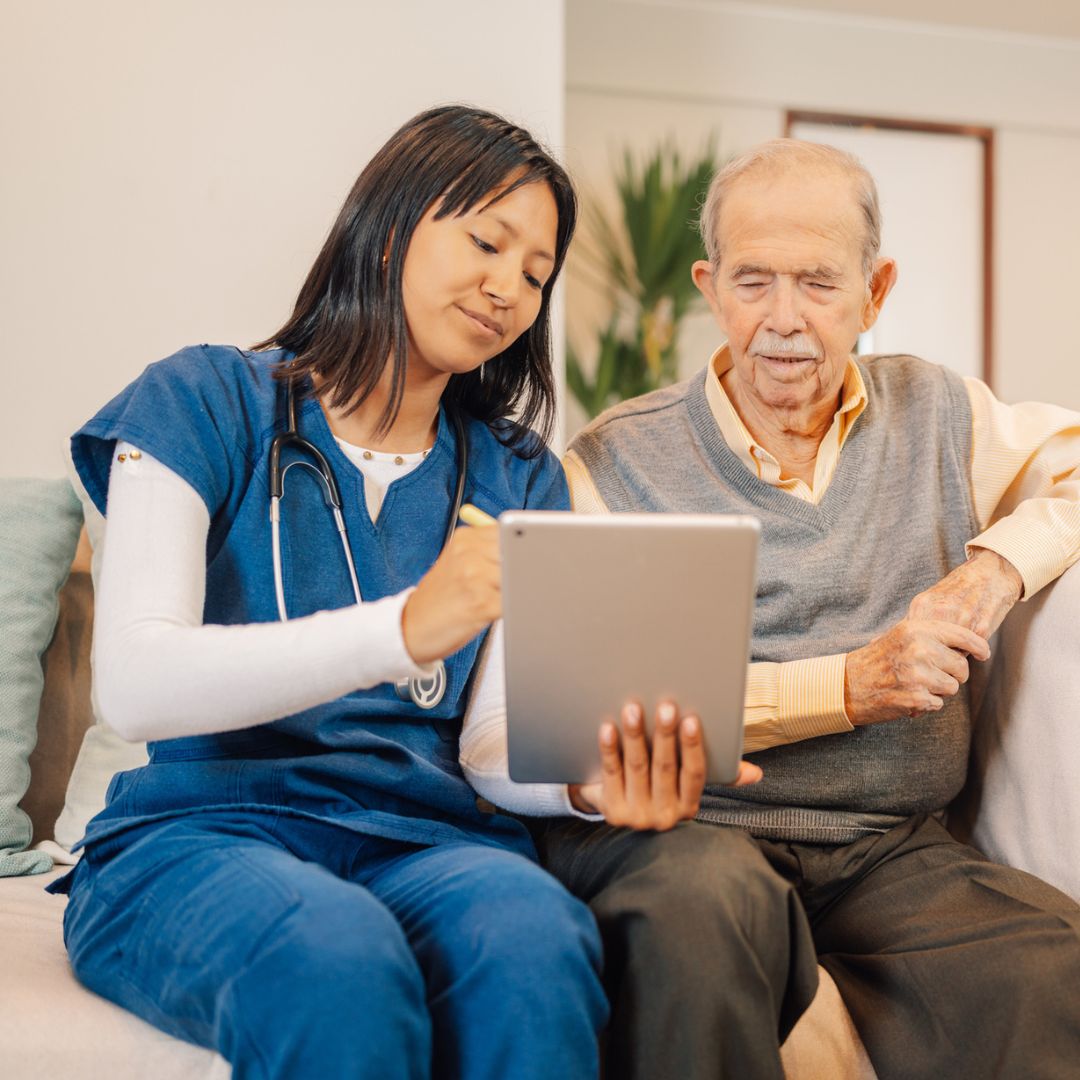 Kvinnelig pleier viser et nettbrett til en eldre mann