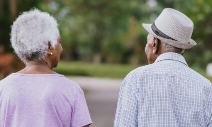 en eldre mann med grå hatt og en eldre kvinne i rosa skjorte på spasertur