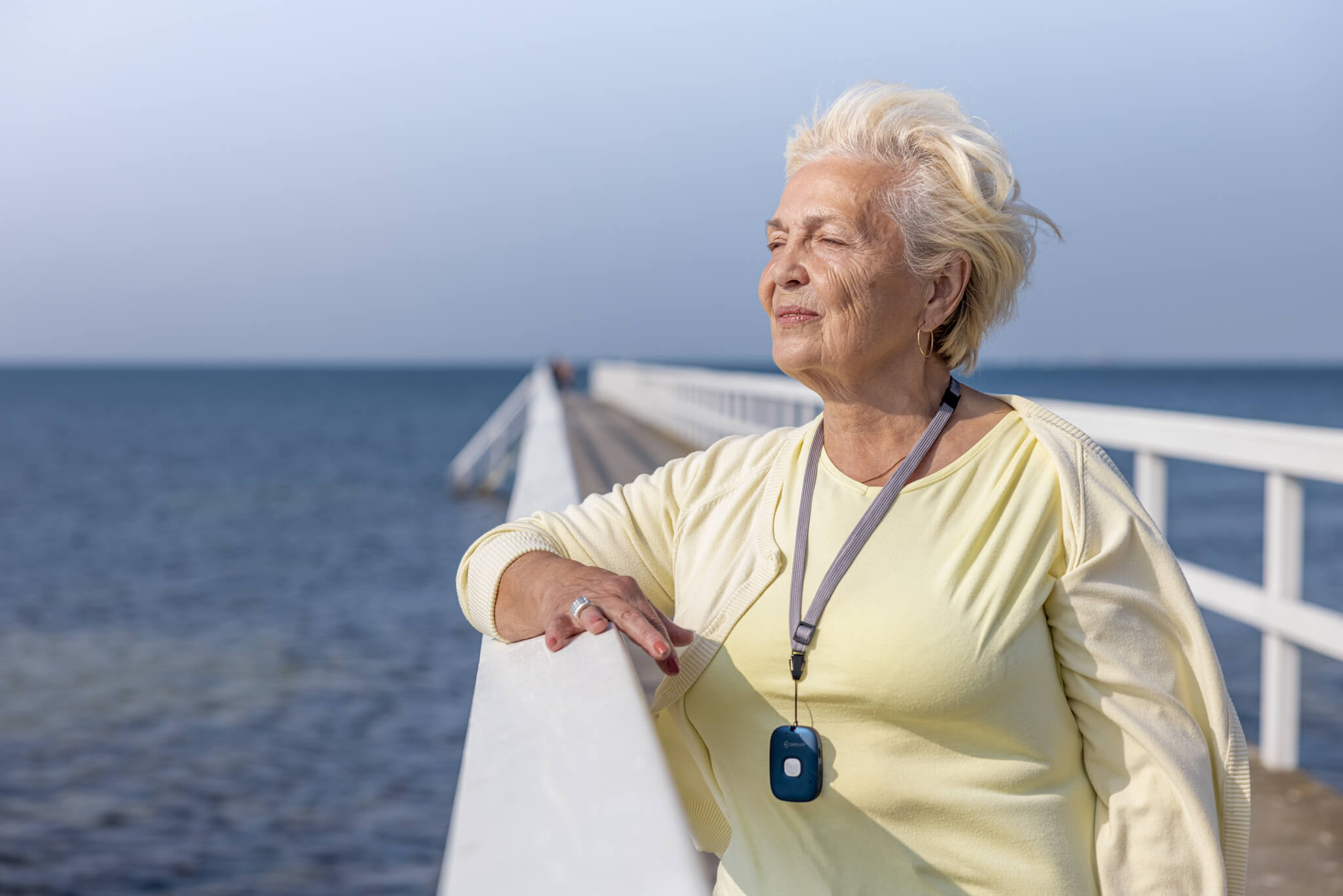 Elderly woman on pier looking out over the ocean, wearing Abby mobile social alarm