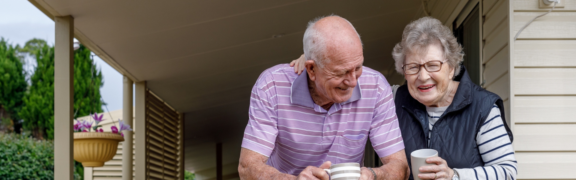 old couple standing on a porch drinking coffee and laughing