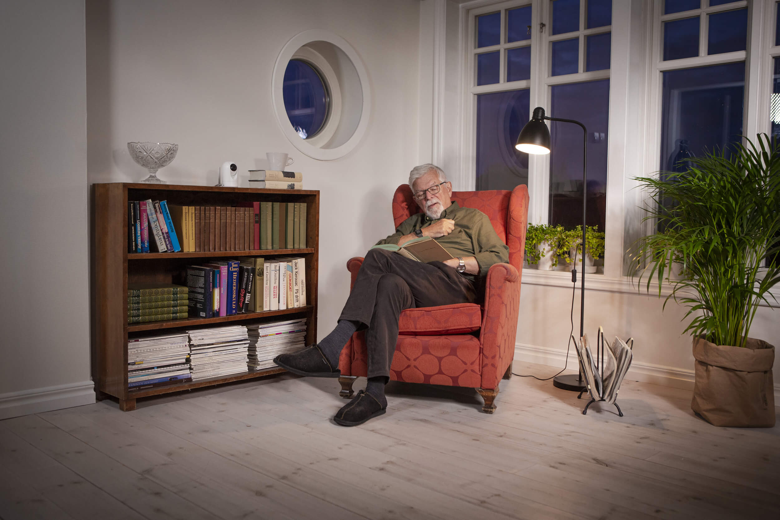 Oudere man in fauteuil die een boek leest met Doro Visit camera op de boekenkast.