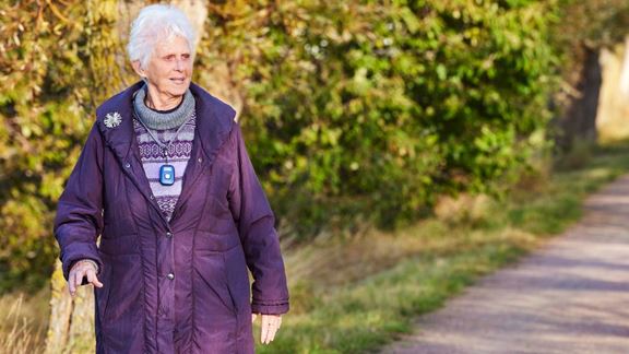 Äldre dam på promenad längs all+en med sitt mobila trygghetslarm om halsen