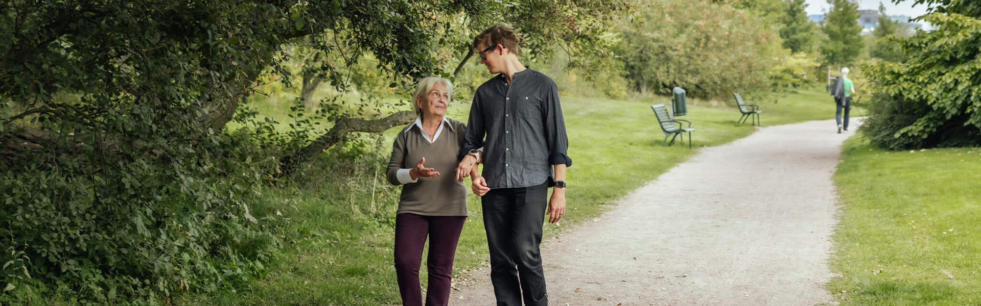 Äldre kvinna och yngre man promenerar i en park.
