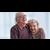 Two seniors sitting on a couch laughing and holding hands