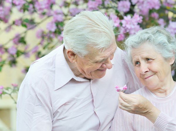 Äldre par som ler med blommor i bakgrunden