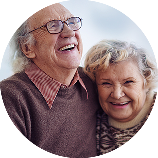 Zwei ältere Menschen sitzen lachend auf einer Couch und halten sich an den Händen