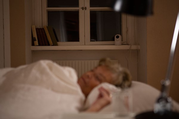 Femme senior endormie dans son lit avec caméra Doro Visit en arrière-plan