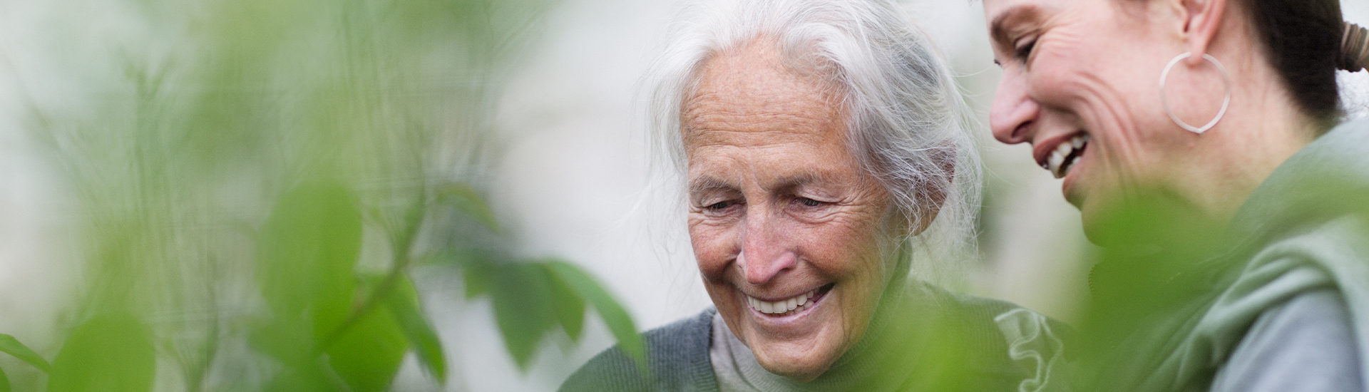 Ältere Person und junge Frau lachen mit Pflanzen im Vordergrund