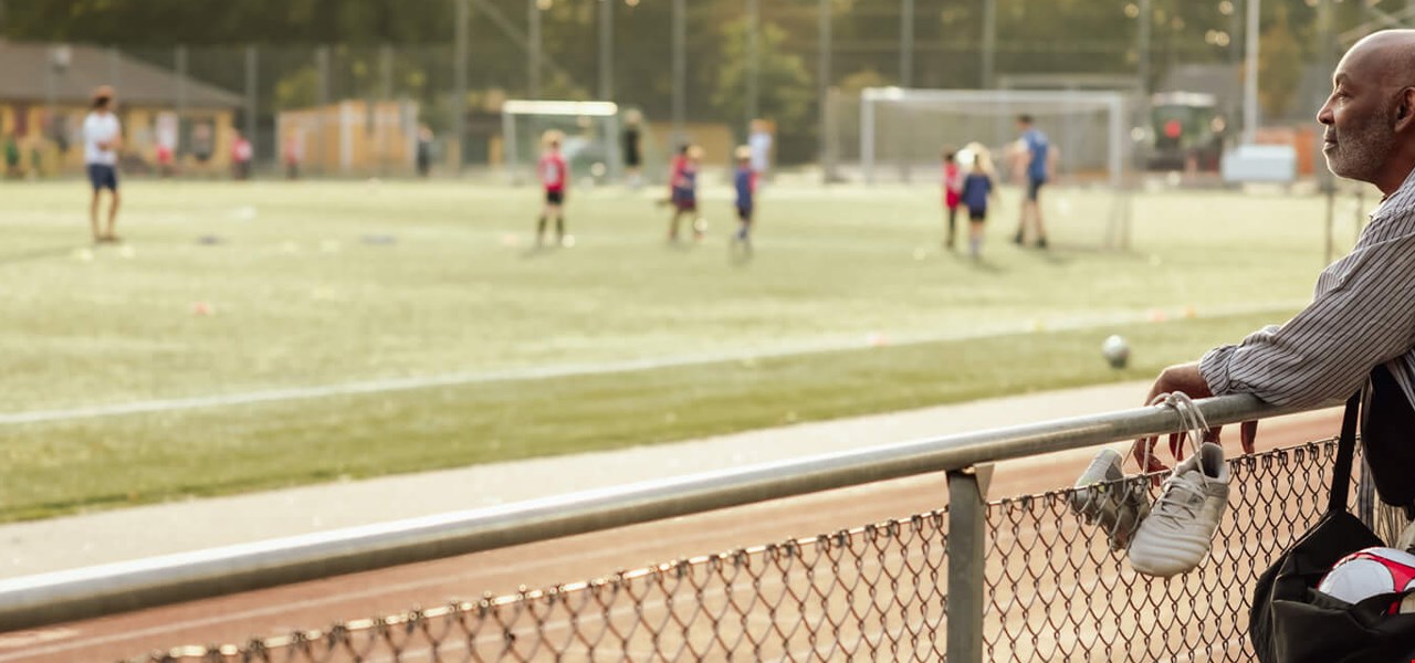 Man standing by a football field, looking at players.