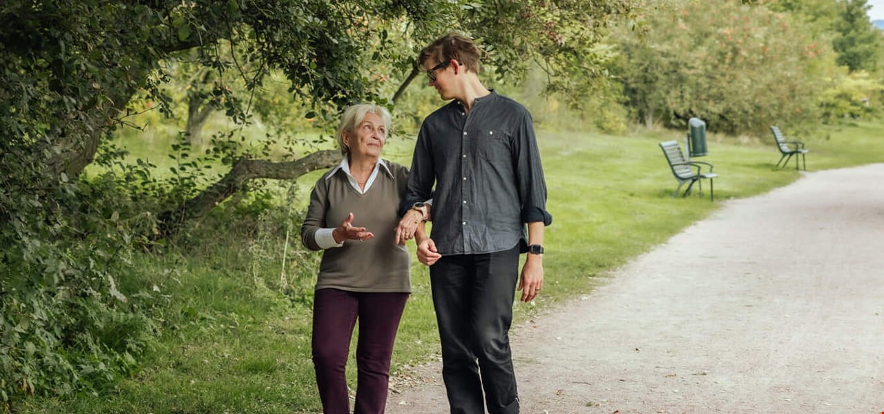 Senior woman and young man walking in park.